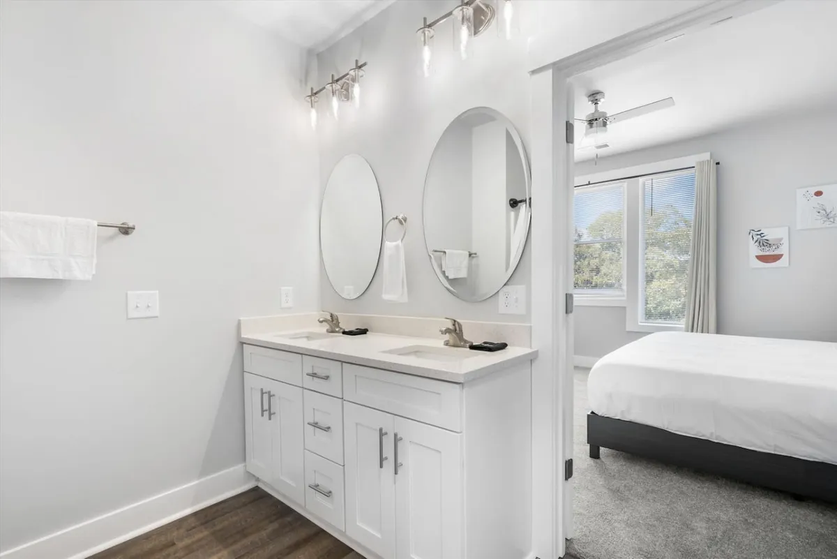 A bright bathroom with a double sink vanity, mirrors, and modern light fixtures illuminated by natural light from a window—ideal for morning routines and relaxation.