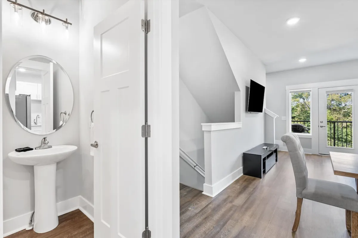 A modern, inviting interior featuring a dining table, sleek sink, mirror, staircase, and a TV. The space is well-lit and designed for both relaxation and work, suggesting areas suitable for dining, casual meetings, or catching up on emails.