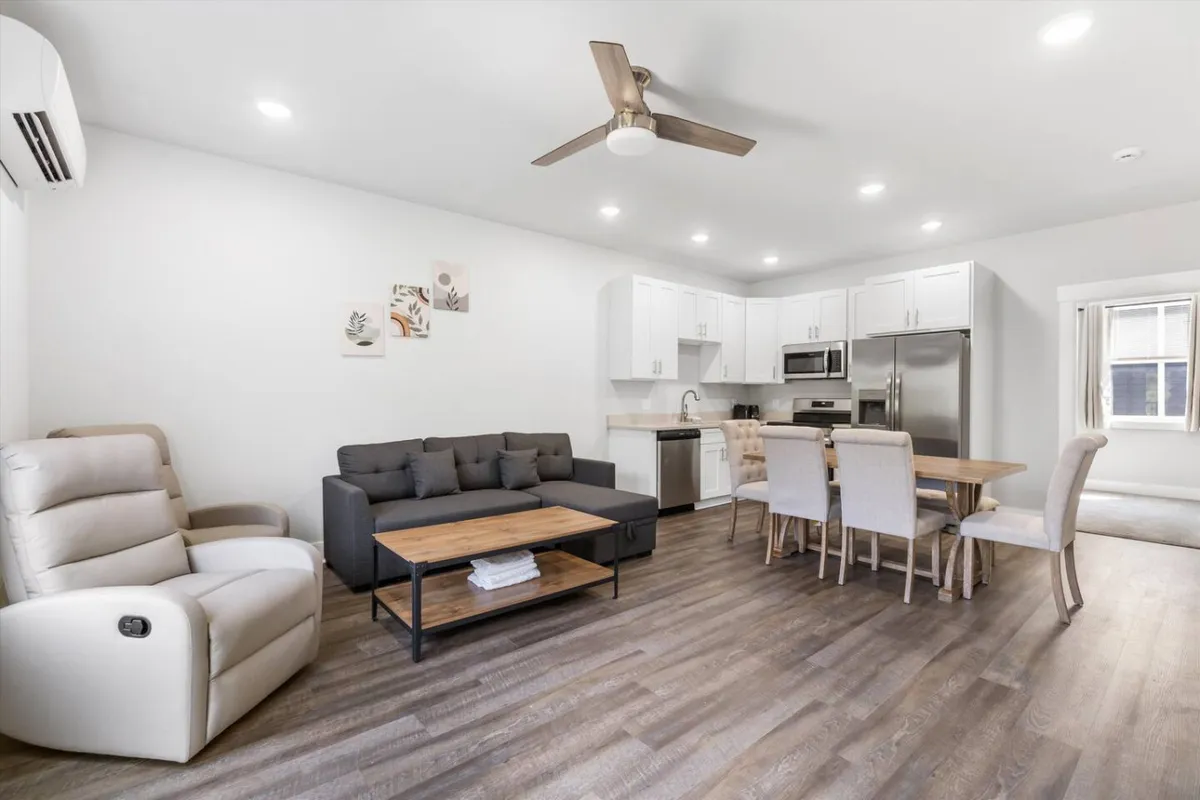 A cozy, modern open-plan living and dining area featuring a comfortable sofa, a dining table, kitchen appliances, and decorative artwork. The space is designed for relaxing, sharing meals, and entertaining, with a warm and inviting atmosphere that feels like home.