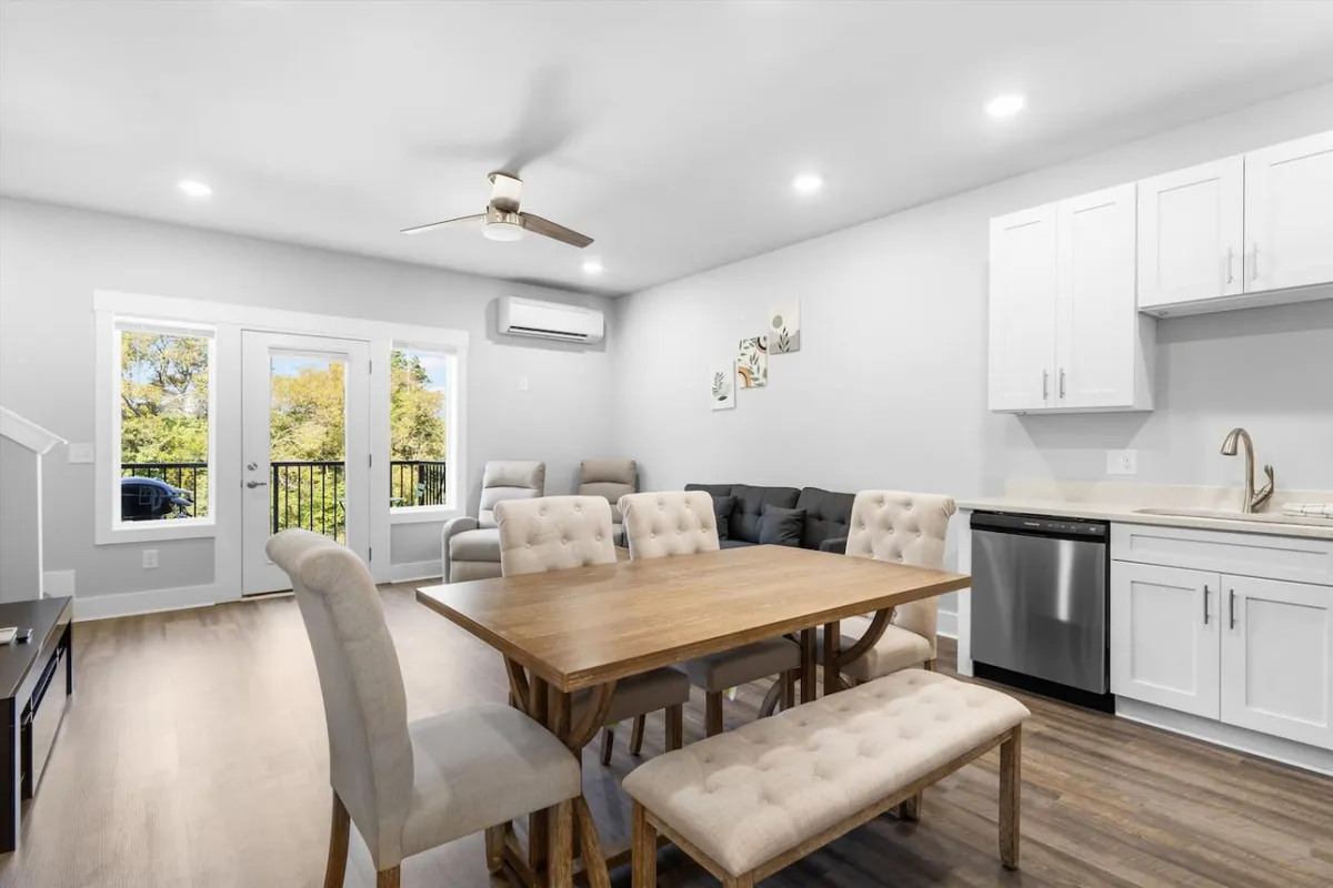 A cozy living and dining area bathed in natural light from large windows. The arrangement includes a plush sofa and a welcoming dining table, suggesting a space ideal for relaxation, conversation, and enjoying quiet moments as a group.