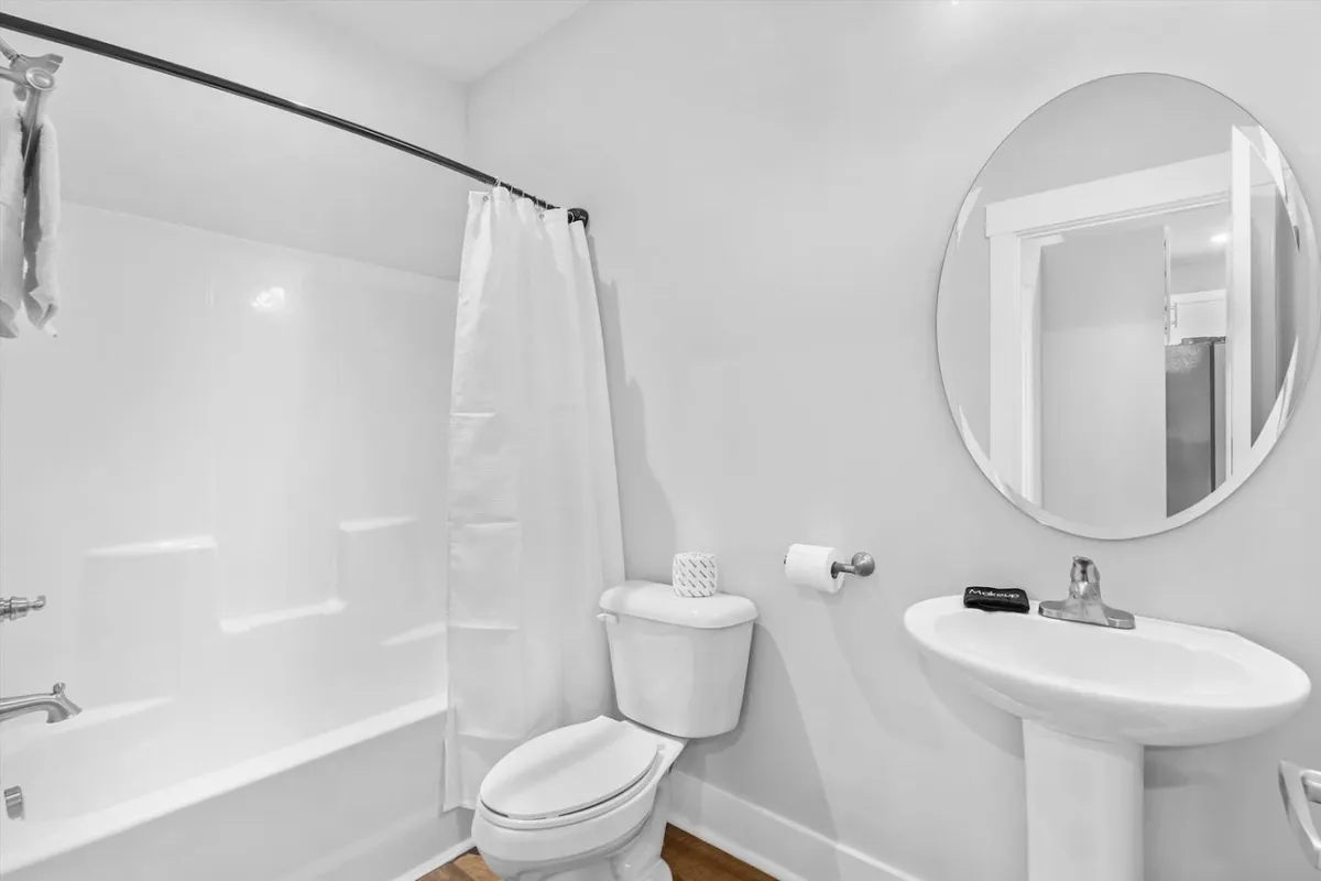 A calm and refreshing shared bathroom with a large mirror, shower curtain, sink, and toilet. The design is functional yet inviting, ideal for guests staying in the second floor king bedroom.