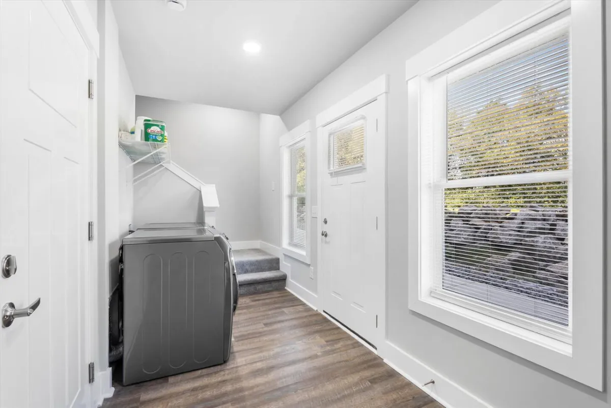 This image shows a functional interior scene with the washer and dryer prominently placed near the front door and windows. The space is bright and organized, suggesting both utility and a welcoming entrance. Elements like laundry supplies, a clear pathway from the entry, and opportunities to organize belongings are visible.
