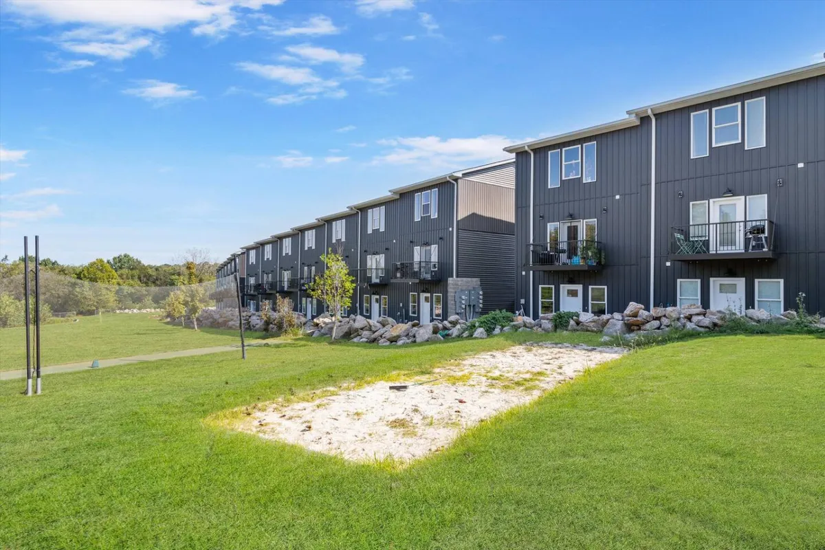 An exterior shot showcasing a vibrant green lawn, modern apartment building, and a sand area for play. The setting is lively and welcoming, perfect for families to gather, relax, or let children play safely before heading out to Nashville's legendary sites.